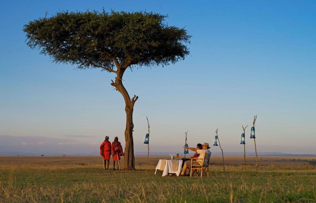 A couple enjoying a sundowner dinner beneath an acacia tree on the Tanzanian savanna
