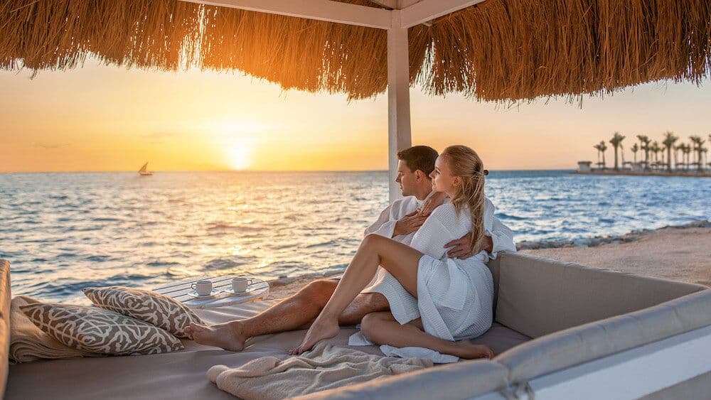 Couple relaxing on a beachside daybed watching the sunset over the Indian Ocean