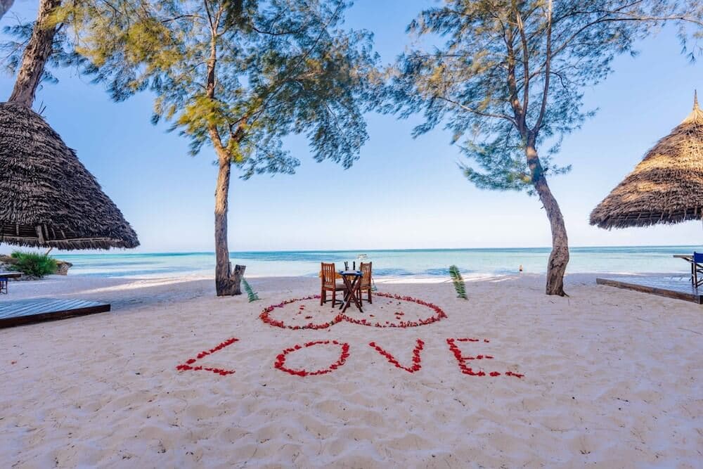 Romantic beach setup with a table for two decorated with rose petals spelling LOVE